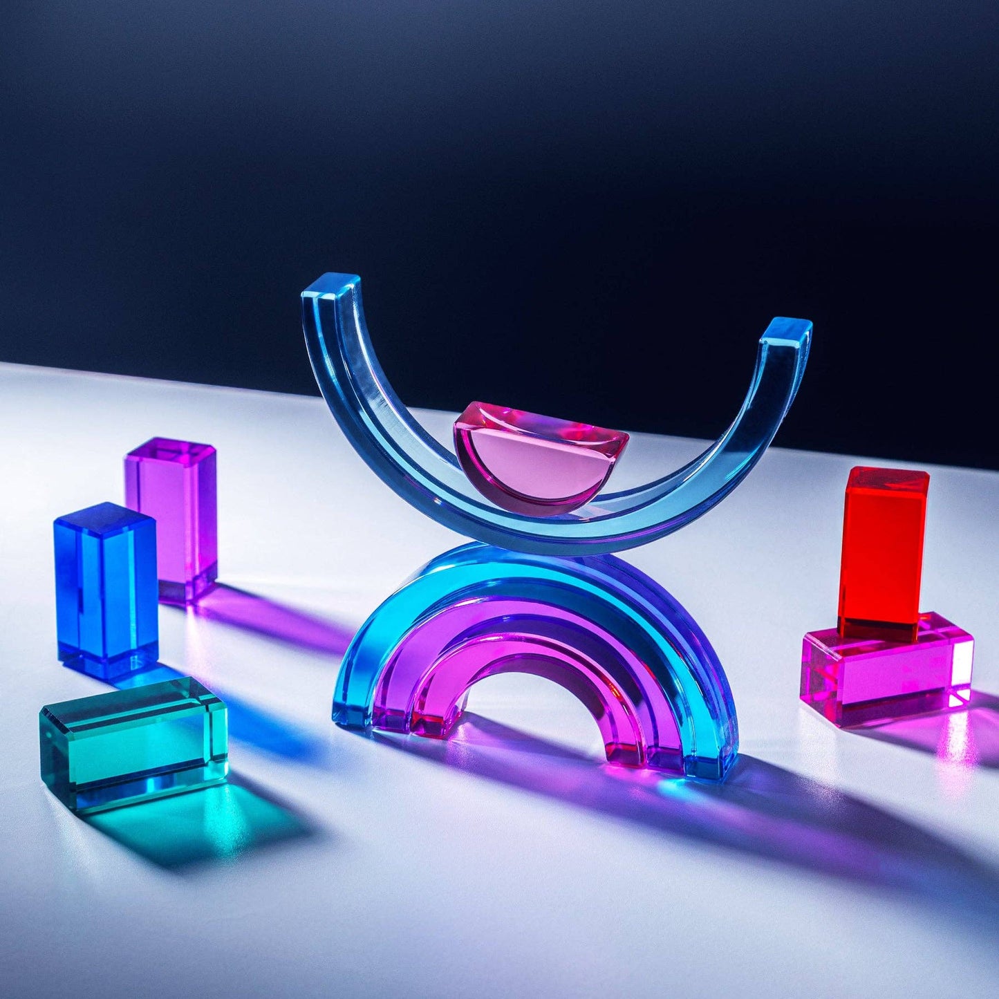 Colorful glass geometric shapes on a reflective surface with a dark background