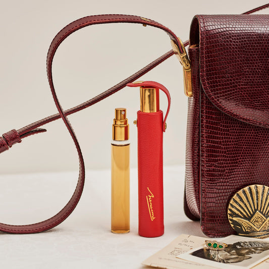 Two perfume bottles and a brown leather handbag on a light surface.