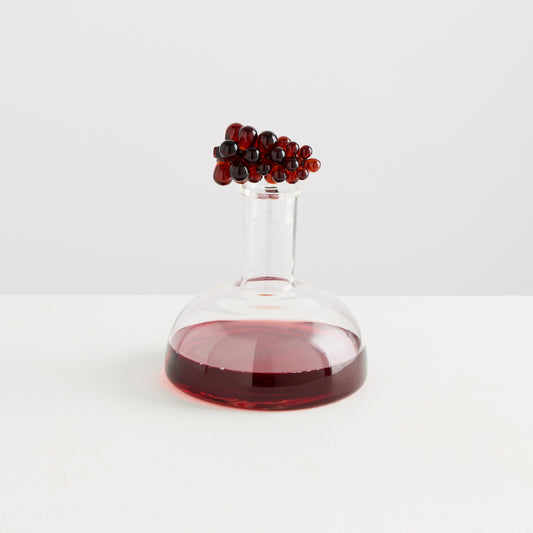 Clear glass decanter with red liquid and decorative elements on a white background