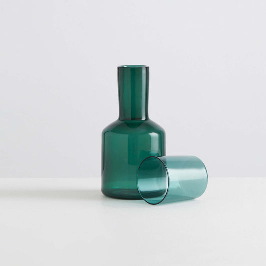 Green glass carafe and tumbler on a light gray background