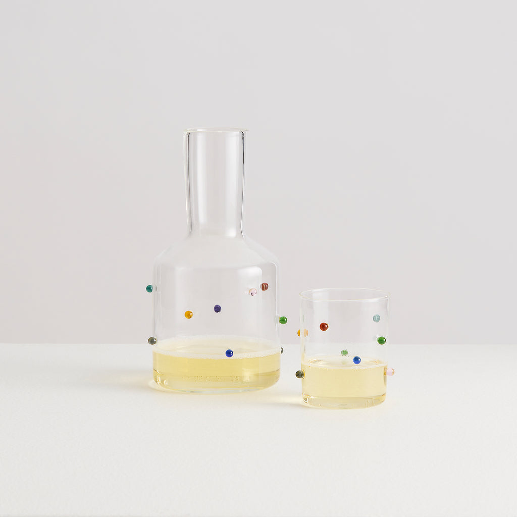 Clear glass carafe and two glasses with colorful dots on a white background
