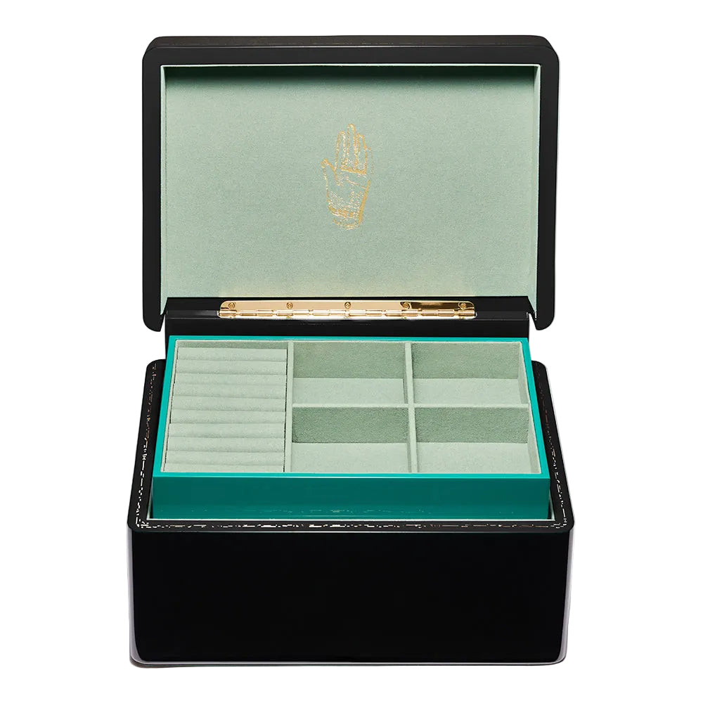 A black lacquered jewelry box with its lid open, showing a mint green velvet interior with a gold crest on the inside lid and multiple compartments.