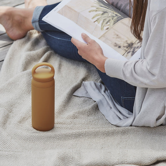 Person reading a book with a mustard yellow water bottle on a blanket