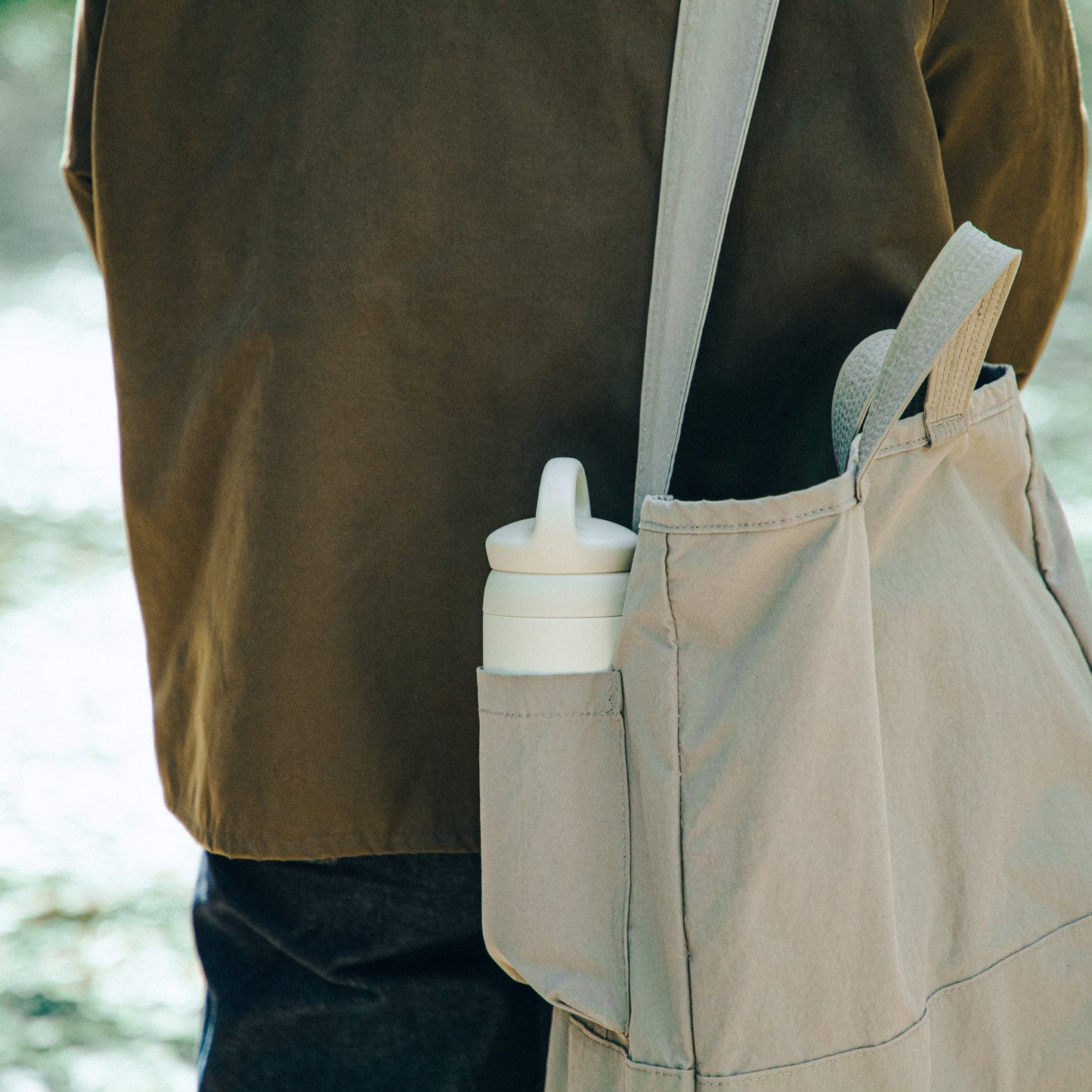 Person wearing a beige apron with a water bottle in a pocket, outdoors.