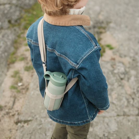 Person wearing a denim jacket with a green thermos bag over one shoulder outdoors.