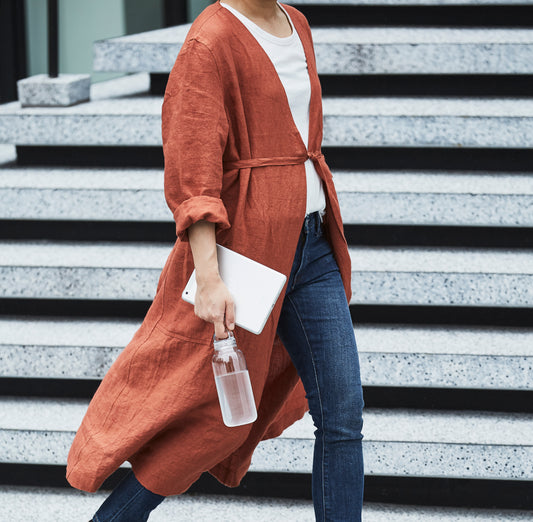 Person wearing a long rust-colored cardigan over a white top and blue jeans, standing on steps.