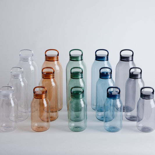 Set of transparent water bottles with colored lids on a light gray background