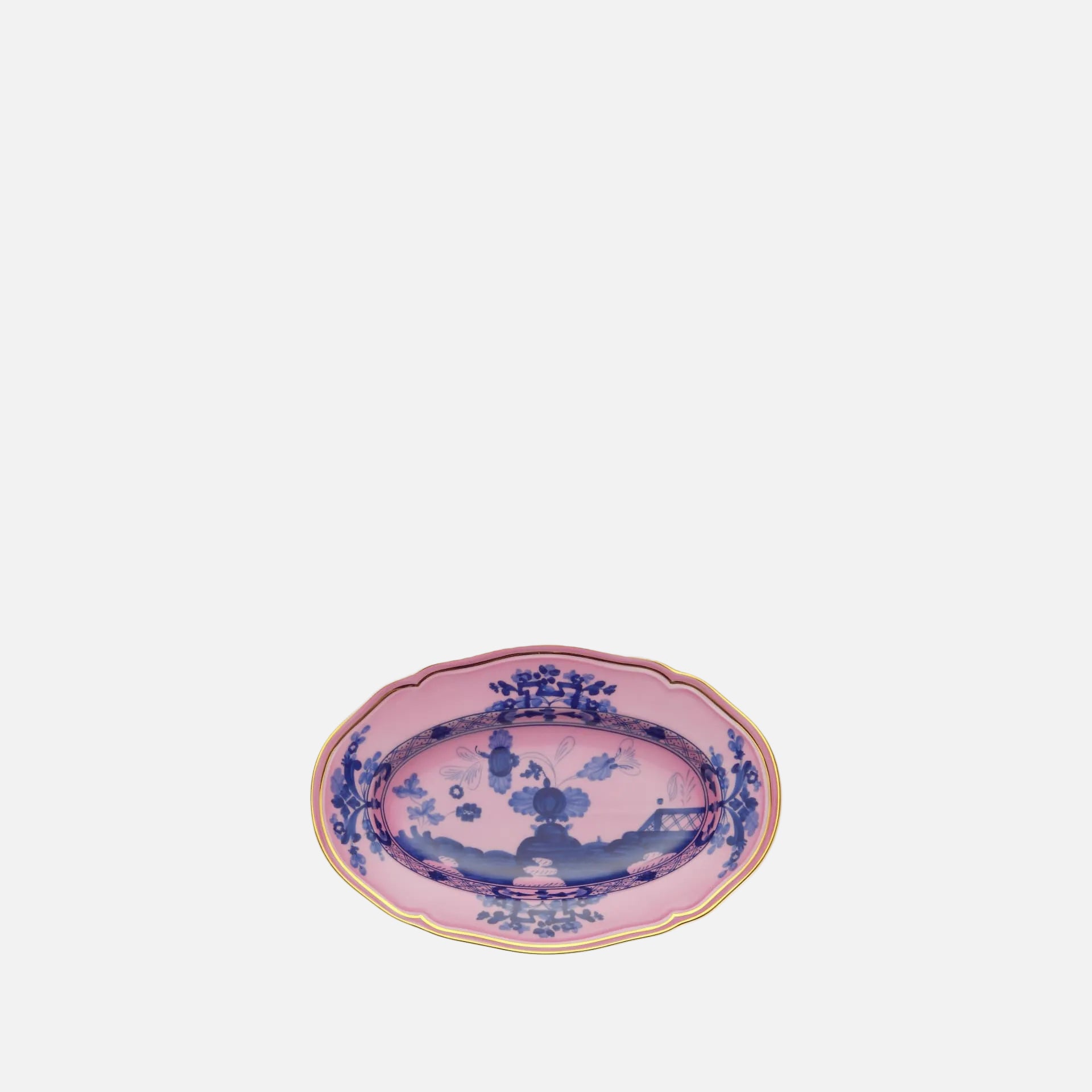 An oval ceramic serving platter with a pink glaze, decorated with blue floral and landscape motifs, and finished with a gold scalloped rim, shown on a plain white background.