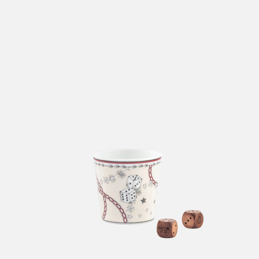 A small white ceramic cup with a red rim and a printed pattern of dice, stars, and chain links, shown on a white background with two small brown wooden dice in front.