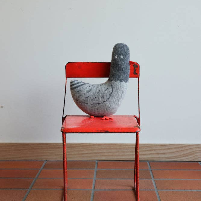 Gray bird-shaped object on a red chair with a plain background
