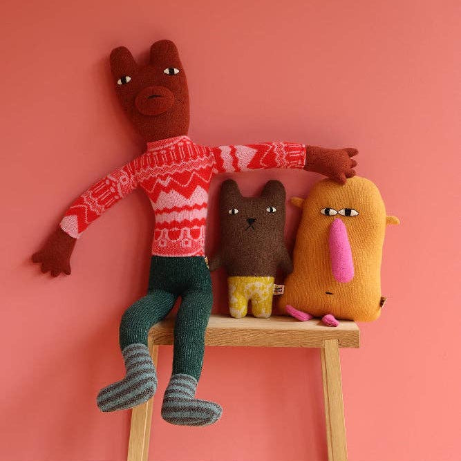 Three plush toys on a stool against a pink wall