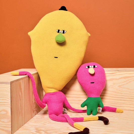 Two colorful plush toys resembling a yellow lemon and pink creature on a wooden surface with an orange background.