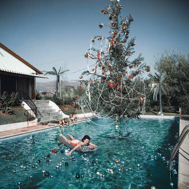 Person floating in a pool with a decorated Christmas tree in the background
