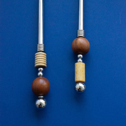 Two stainless steel salad servers with decorative wooden and metal handles, displayed on a solid blue background.