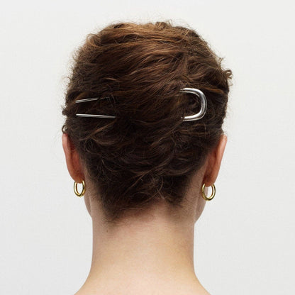Person with hair styled in an updo using two silver hair clips on a plain background