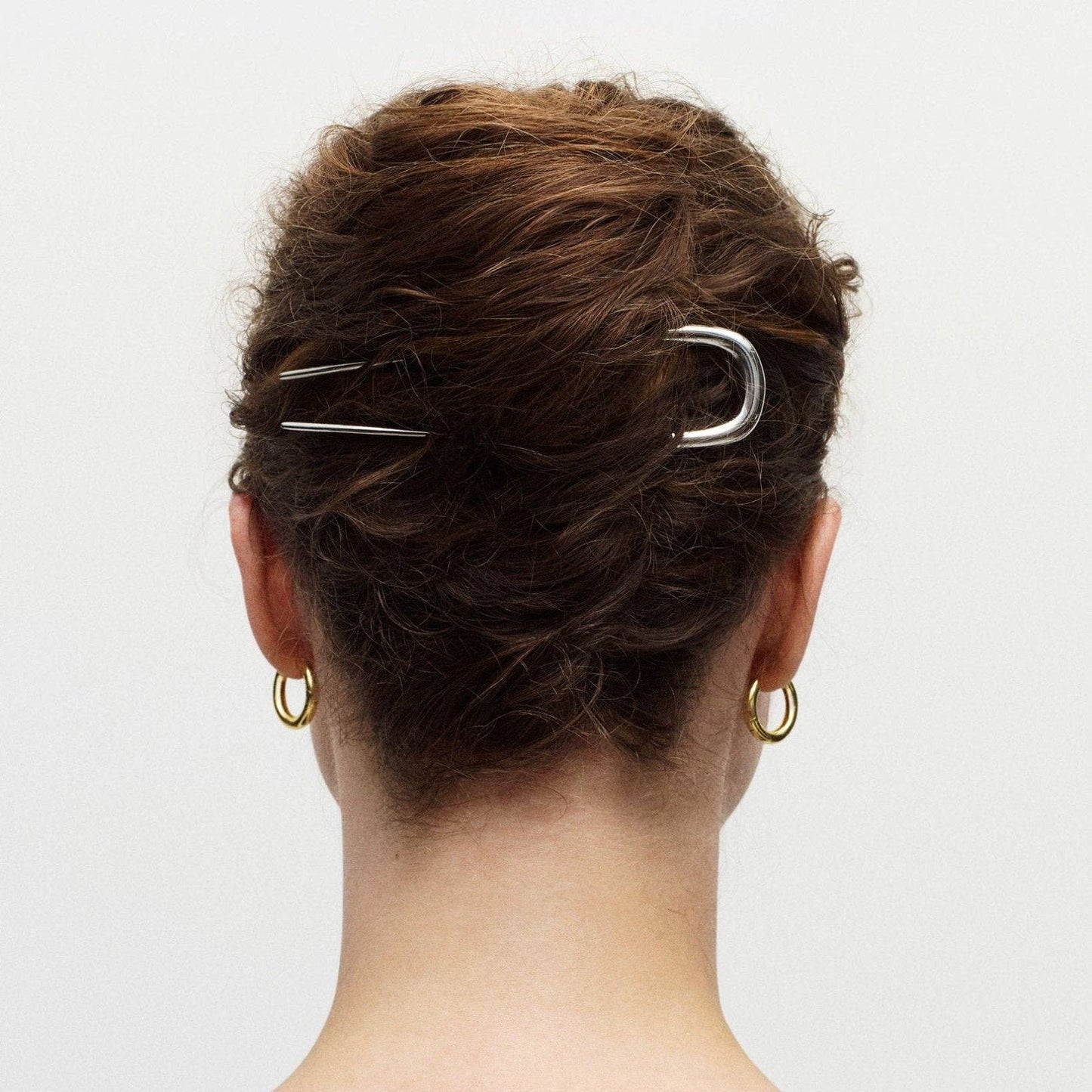 Person with hair styled in an updo using two silver hair clips on a plain background
