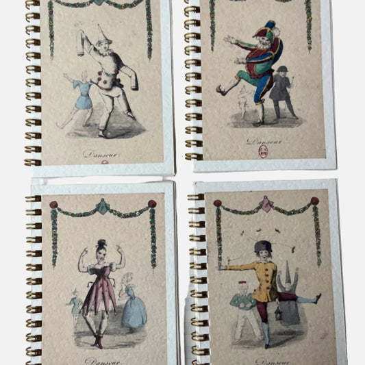Four spiral-bound notebooks with vintage-style illustrations on a checkered surface.