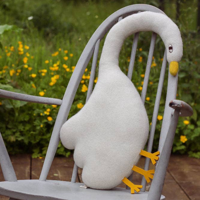 Plush goose toy on a gray chair with a garden background
