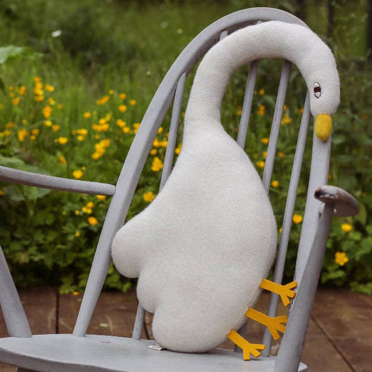 Plush goose toy on a gray chair with a garden background