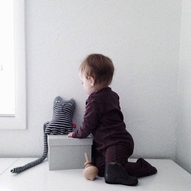 Child sitting on a white surface with a striped toy and gray box against a light gray wall.
