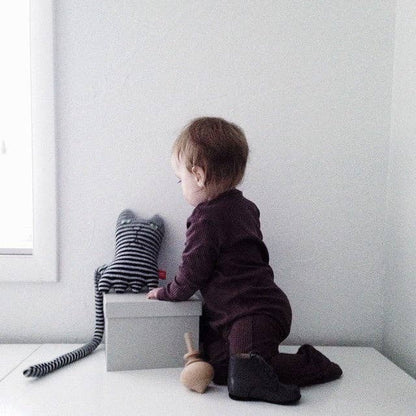 Child sitting on a white surface with a striped toy and gray box against a light gray wall.