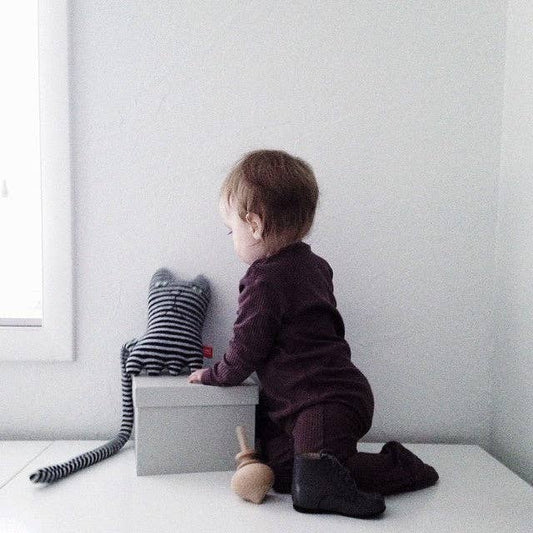 Child sitting on a white surface with a striped toy and gray box against a light gray wall.
