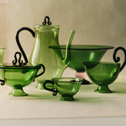 Collection of green glass pieces including a teapot, cups, and bowls on a neutral background