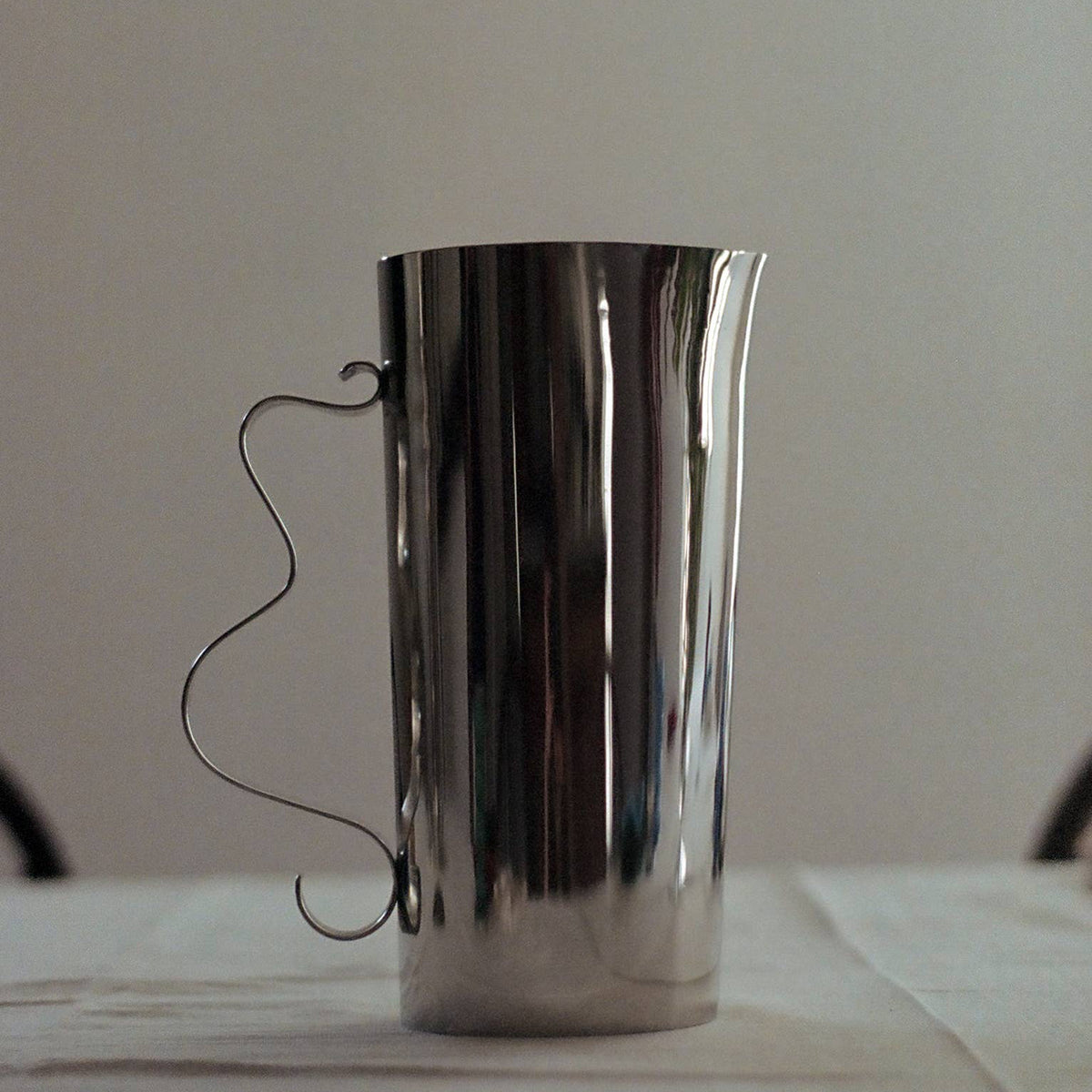Silver pitcher on a white surface with a plain background