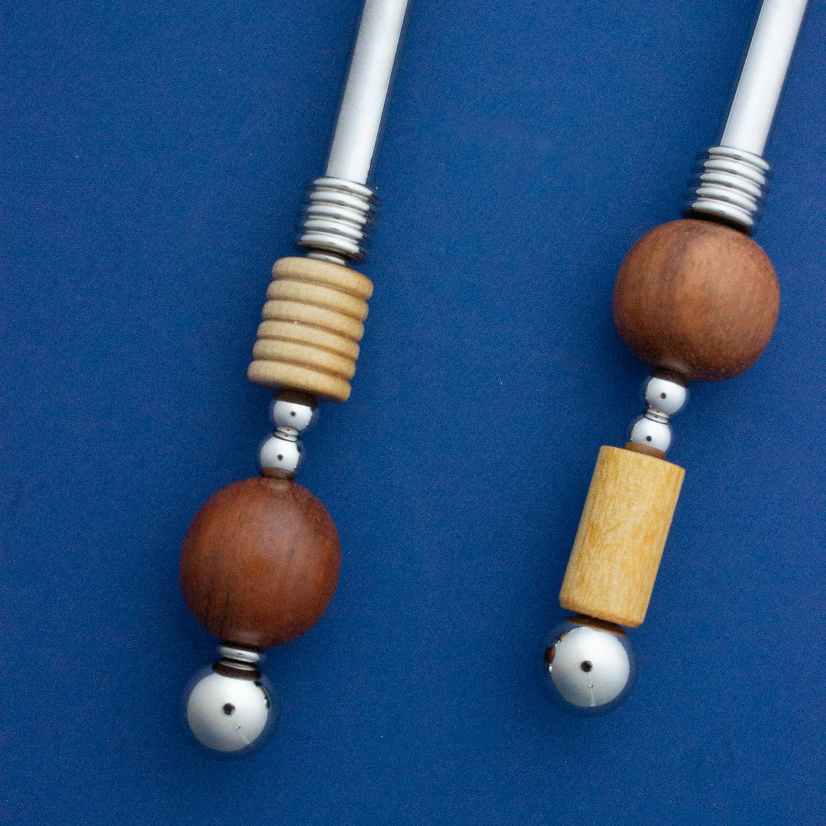 Two beaded dance sticks with white shafts, wooden beads, and silver metal accents, displayed on a solid blue background.