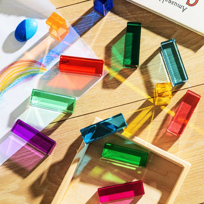 Colorful transparent blocks on a wooden surface with a rainbow and 'Colors' book in the background.