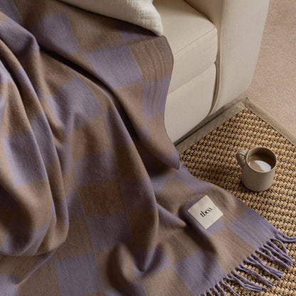 Plaid blanket draped over a sofa with a mug and small container on a textured rug.
