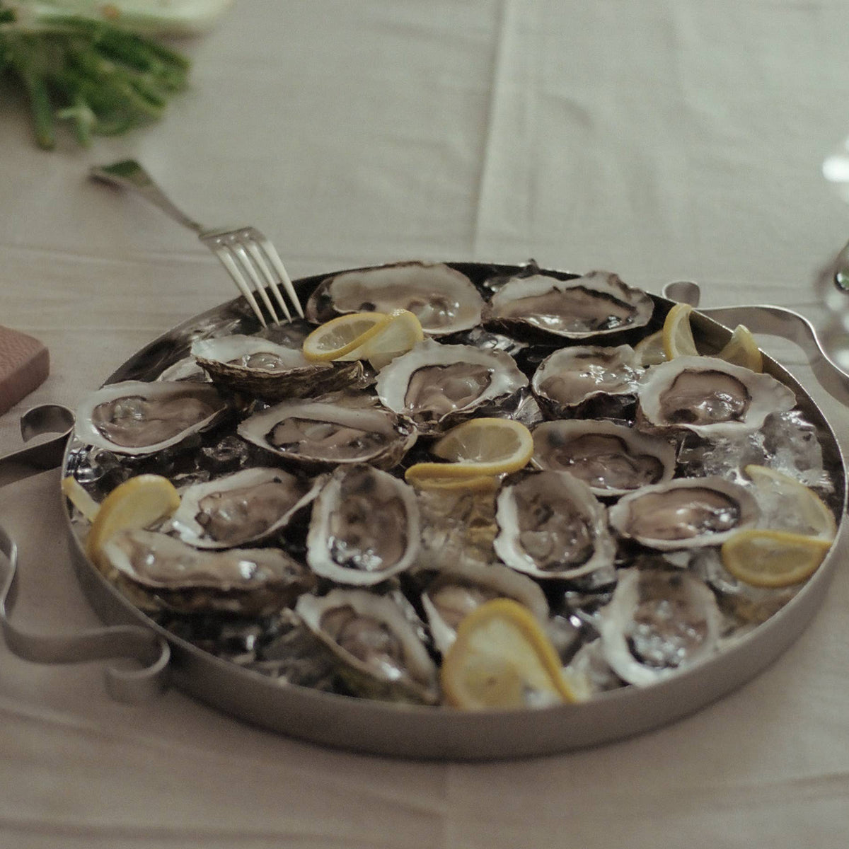 Platter of oysters on a bed of ice with lemon wedges on a table.