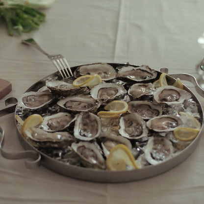 Platter of oysters on a bed of ice with lemon wedges on a table.