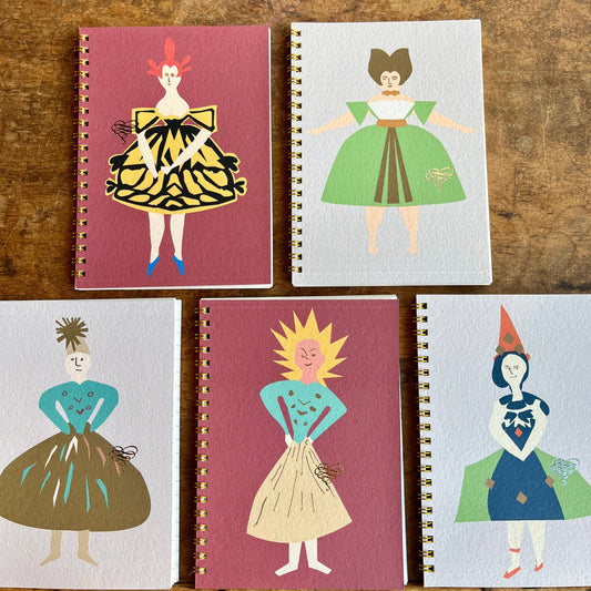 Five notebooks with illustrated covers of people in colorful outfits on a wooden surface.