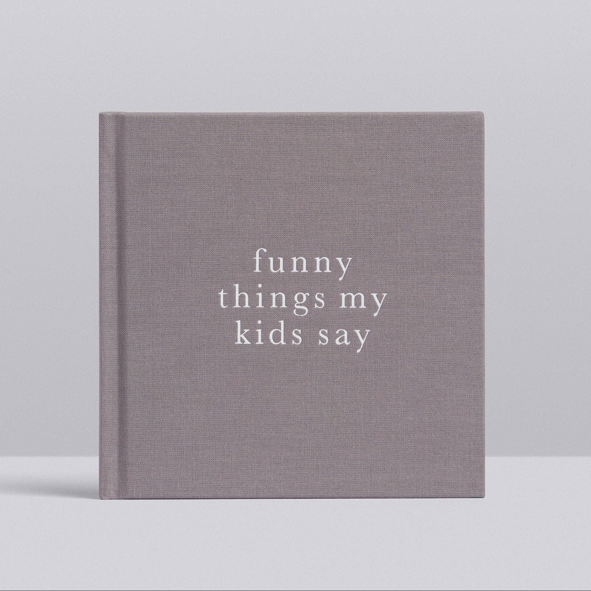 A hardcover book with a textured gray cover and white text reading 'funny things my kids say', photographed against a light gray background.