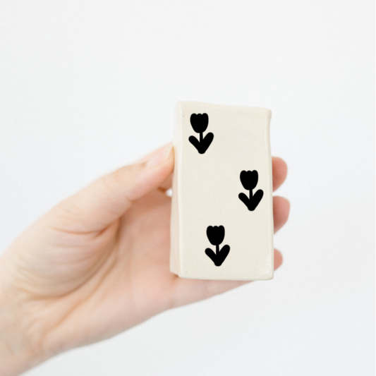 Two hands holding small rectangular objects with black heart designs on a white background