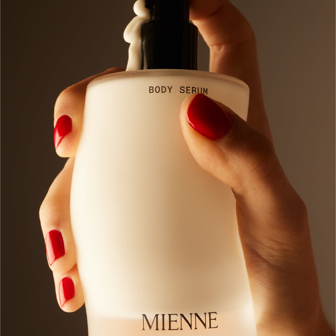 Hand holding a Mienen body serum bottle against a dark background
