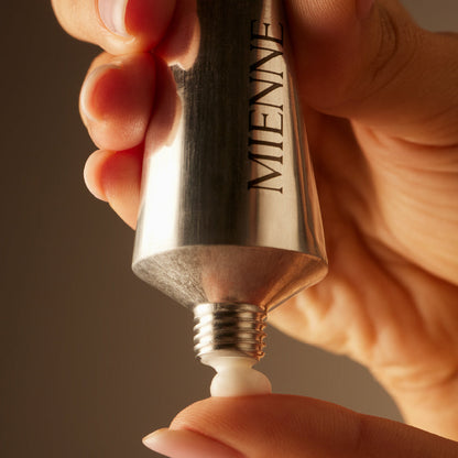 Hand holding a silver Miwene lip balm against a brown background