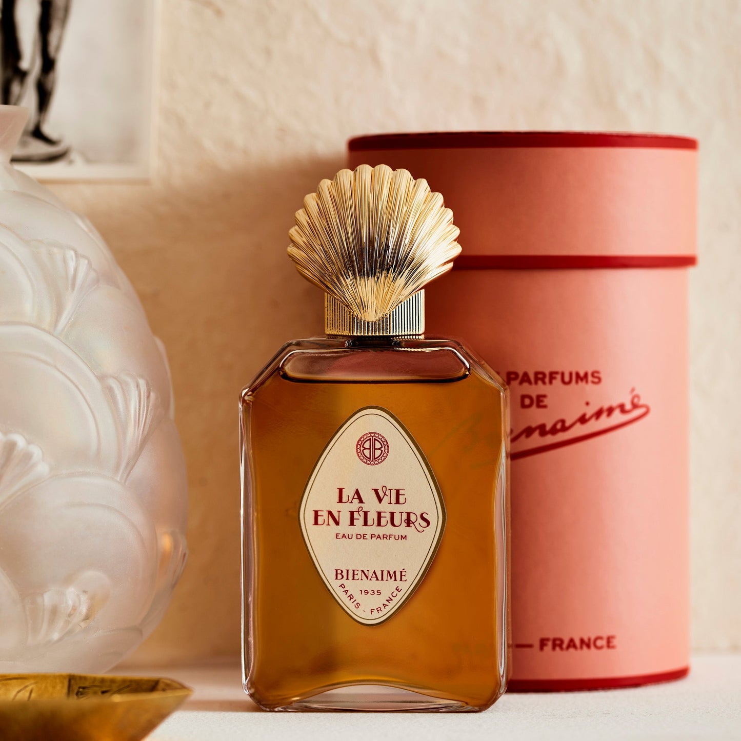 Perfume bottle labeled 'La Vie en Fleurs' by Bienaimé with a pink cylindrical container in the background.