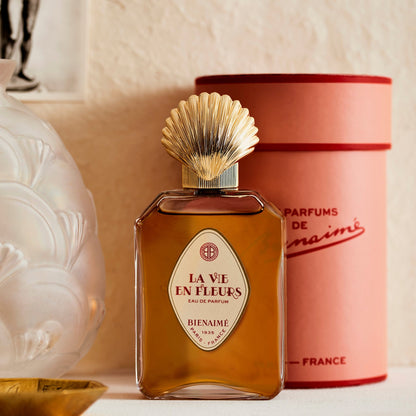 Perfume bottle labeled 'La Vie en Fleurs' by Bienaimé with a pink cylindrical container in the background.