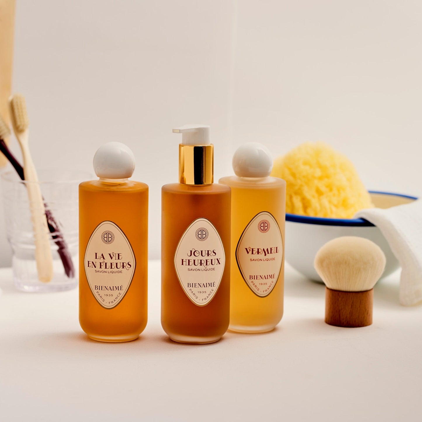 Three bottles of perfume with decorative labels on a white surface, surrounded by bath accessories.