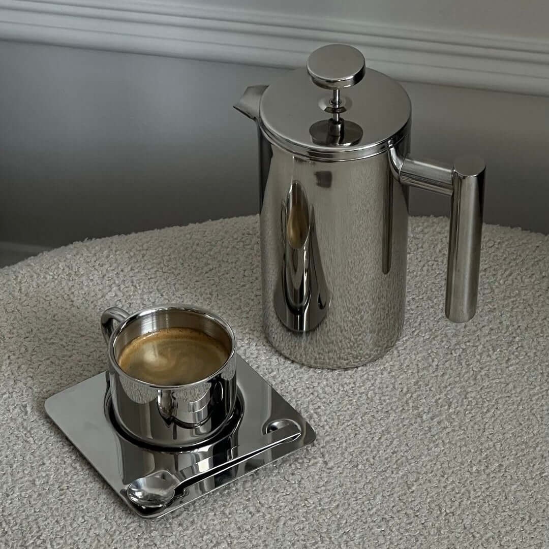 Stainless steel French press with coffee on a mirror tray