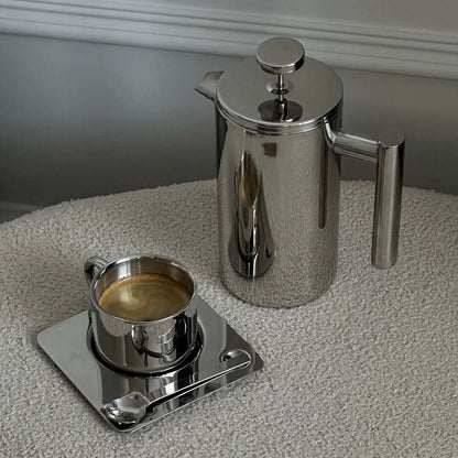 Stainless steel French press with coffee on a mirror tray