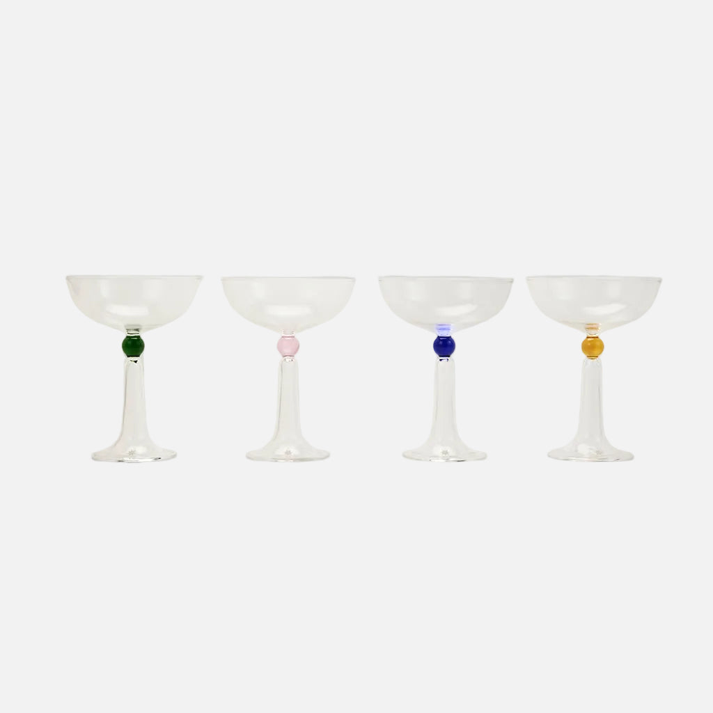 Four cocktail glasses with colored beads on a light gray background
