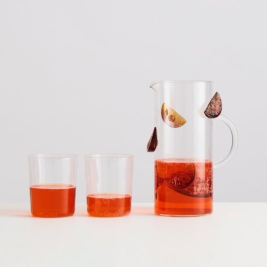 Glass pitcher and two glasses filled with a red liquid on a white background