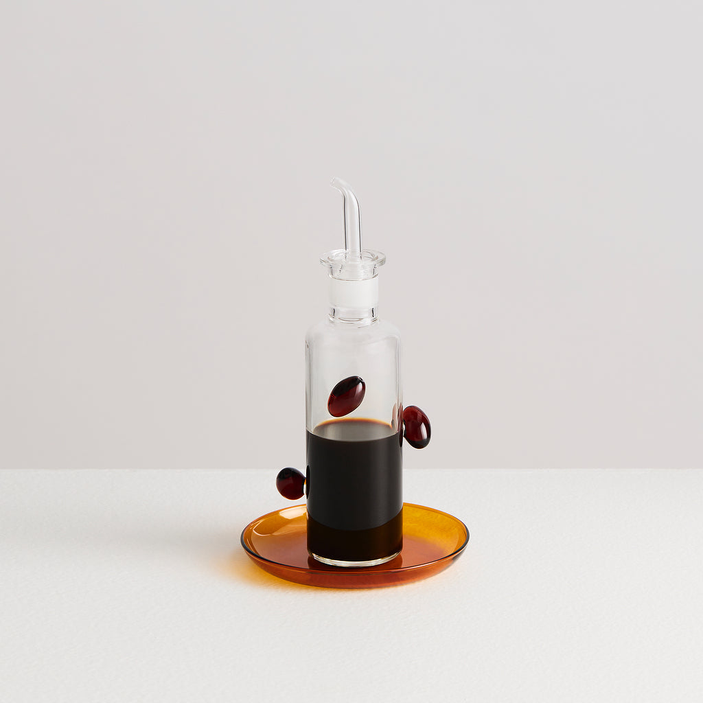 Clear glass bottle with a dropper on an orange dish against a white background