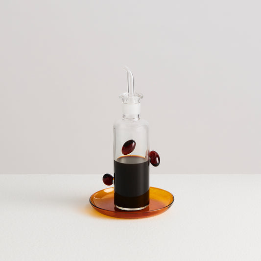 Clear glass bottle with a dropper on an orange dish against a white background