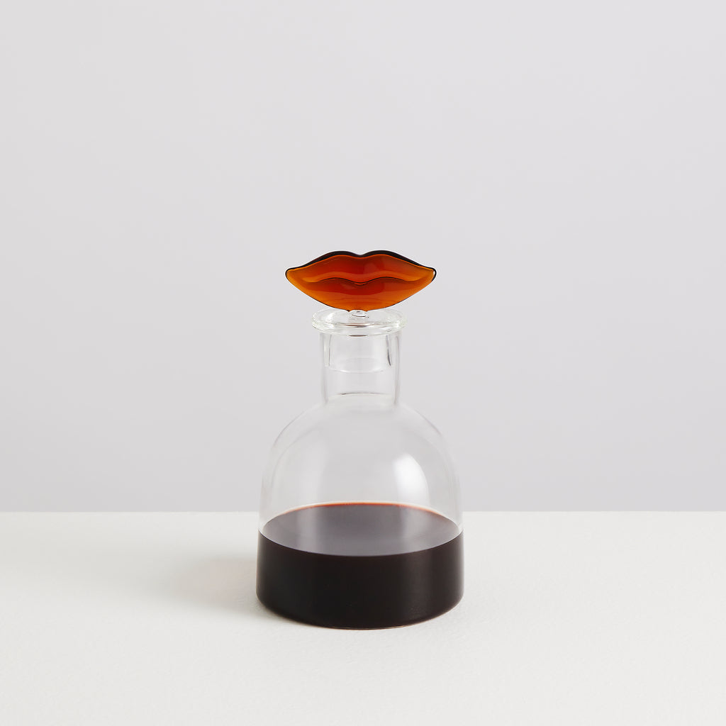 Clear glass carafe with a brown lip-shaped stopper on a white background