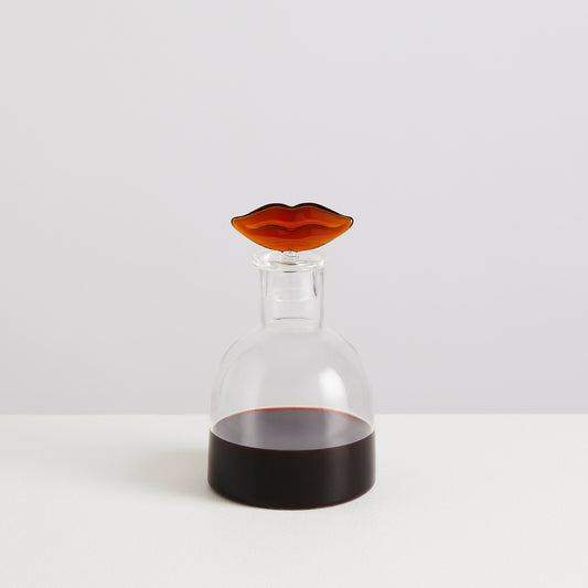 Clear glass carafe with a brown lip-shaped stopper on a white background