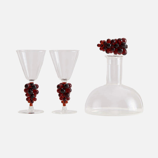 Clear glass decanter and two glasses with grape decorations on a white background